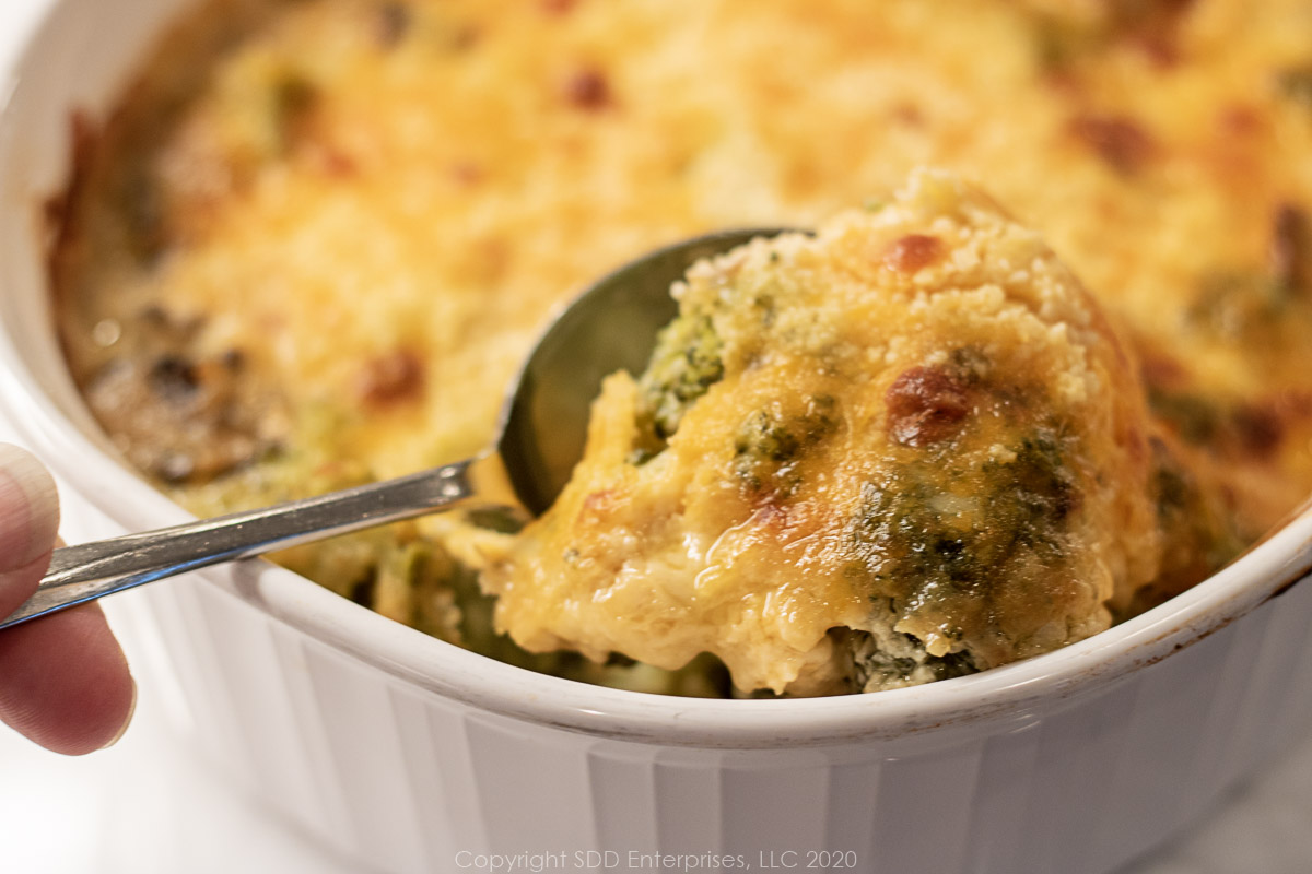 Broccoli casserole in a white baking dish with a serving spoonful