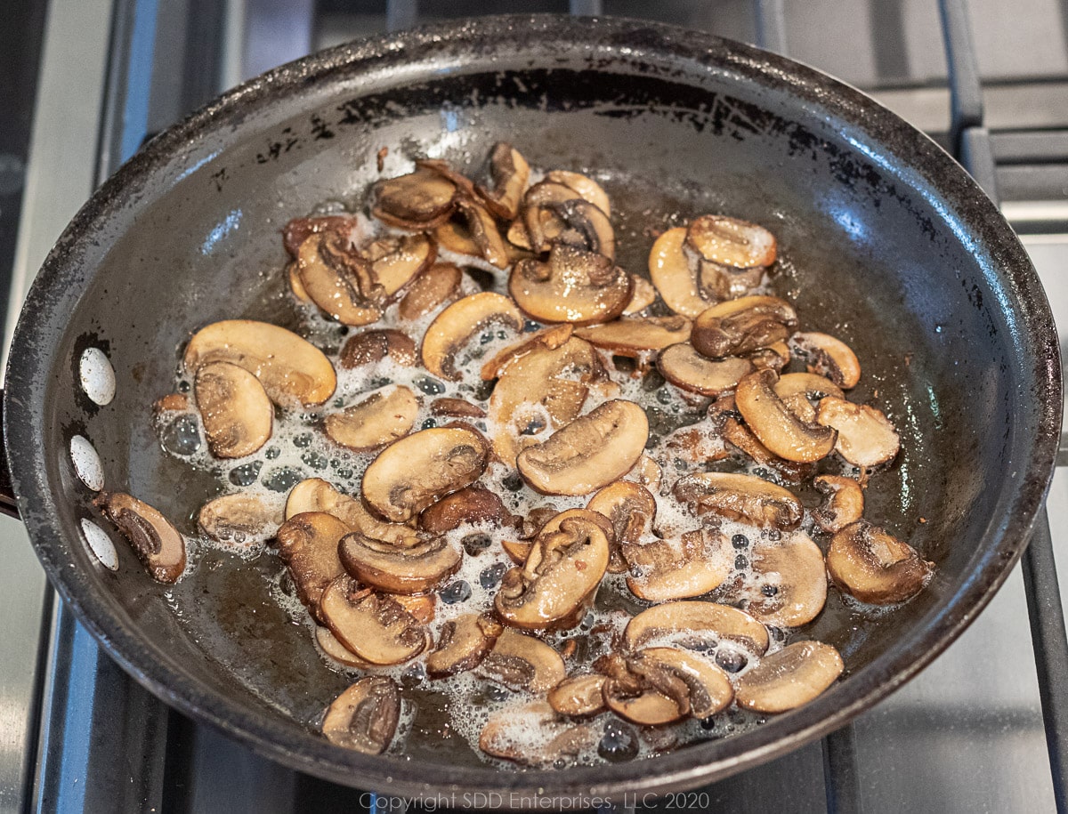 mushroom slices being sautéed in a pan