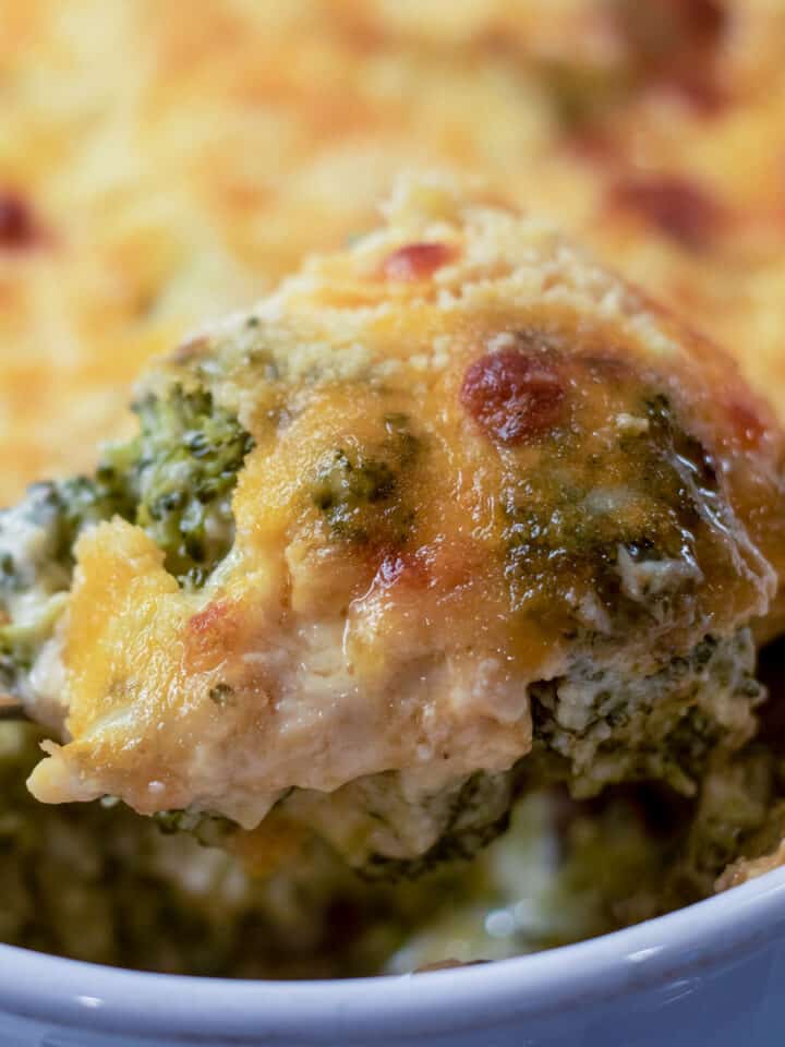 broccoli cheese casserole with a serving spoon in a white baking dish