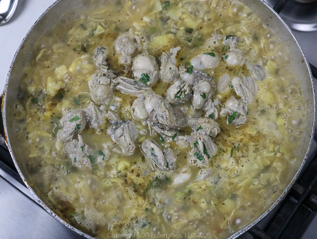 sauteed oysters added to stock and vegetables in a frying pan