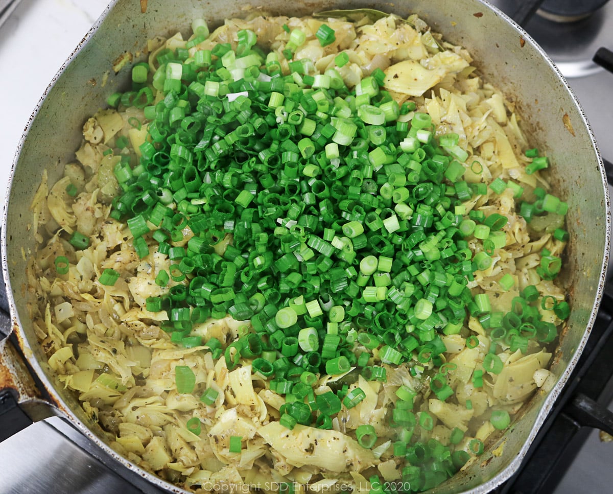 sliced green onions added to sautéed vegetables in a frying pan