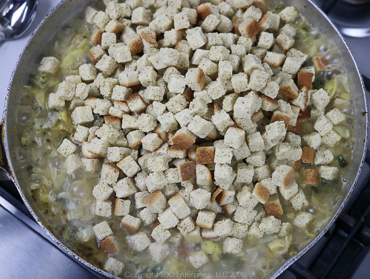 bread cubes added to a skillet with dressing ingredients in a frying pan