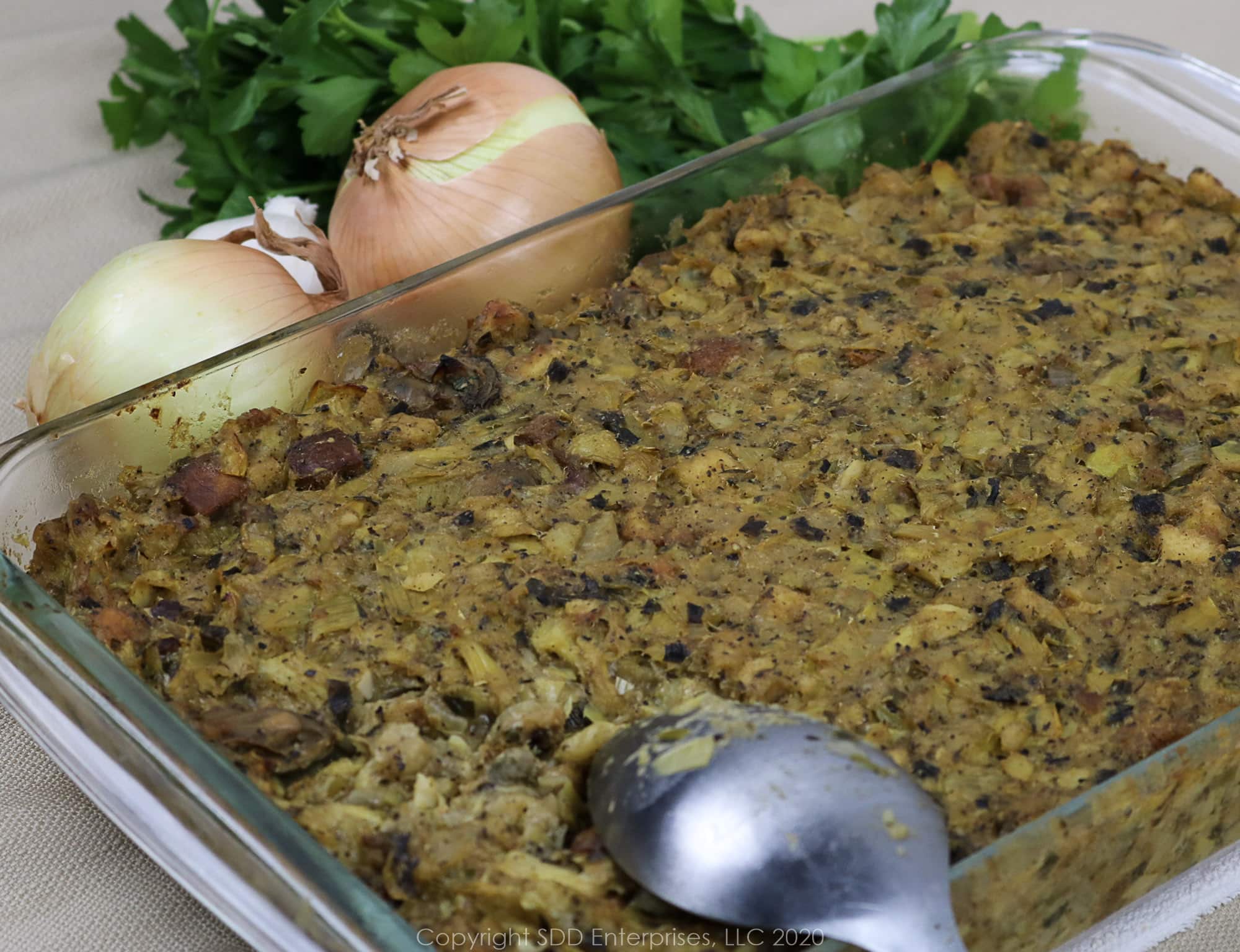 baked oyster artichoke dressing with a serving spoon and vegetable garnish