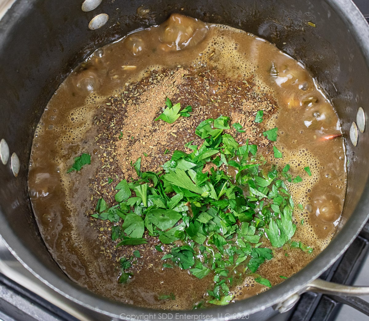 chopped parsley added to seafood gumbo in a stockpot