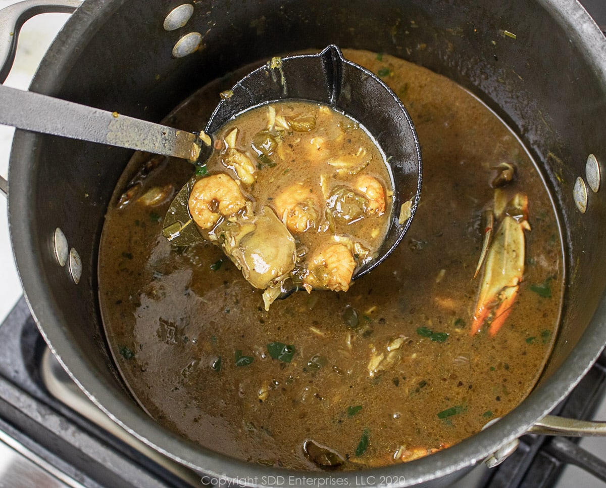 a ladle of seafood gumbo over a stockpot full of gumbo