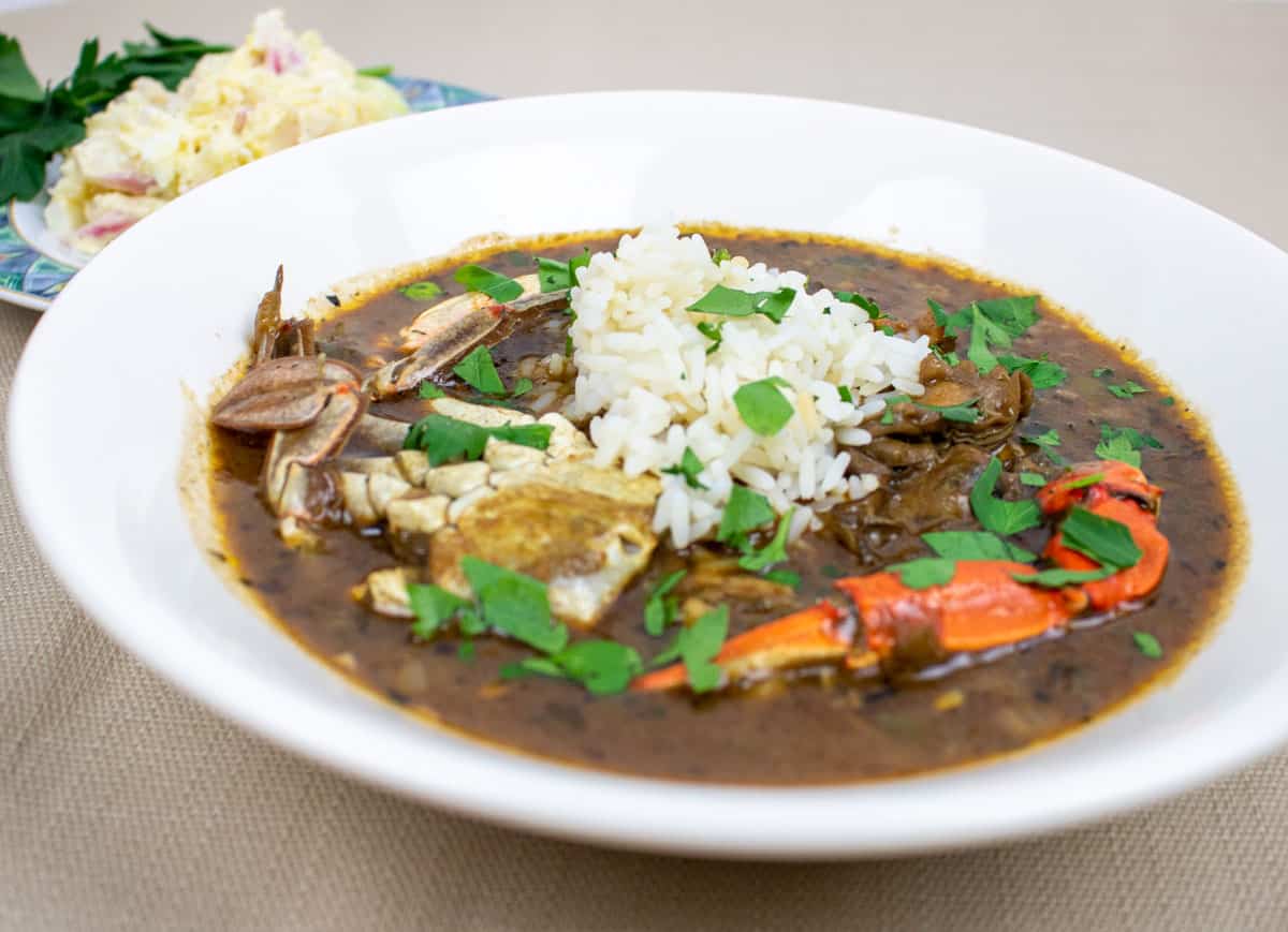 seafood gumbo with rice in a white bowl with potato salad on the side