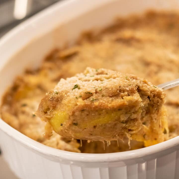 spoonful of yellow squash casserole in a white baking dish