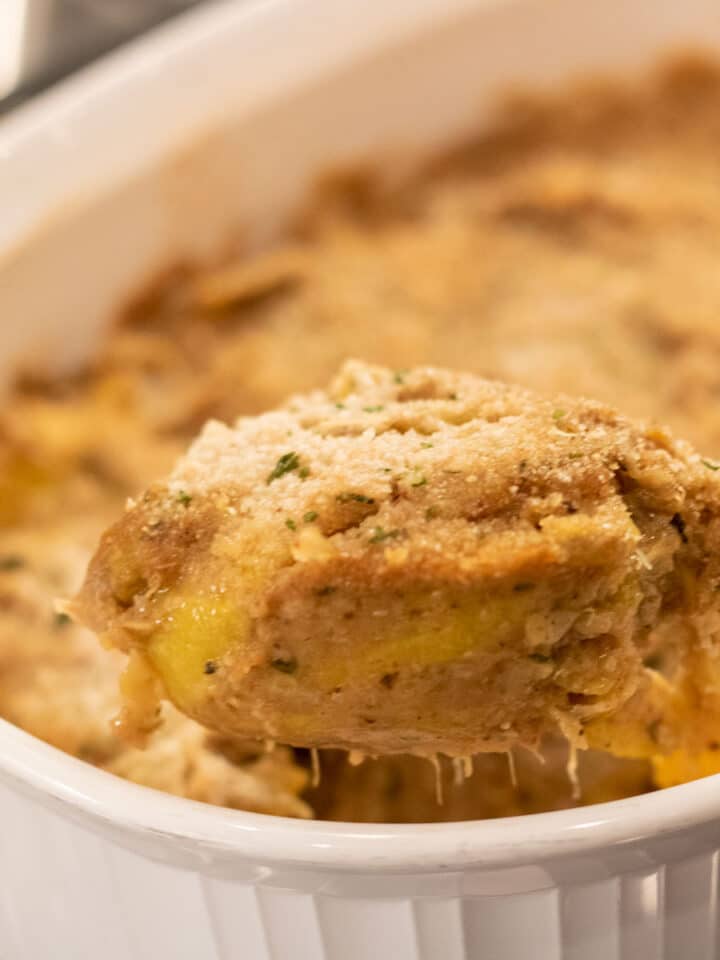 spoonful of yellow squash casserole in a white baking dish