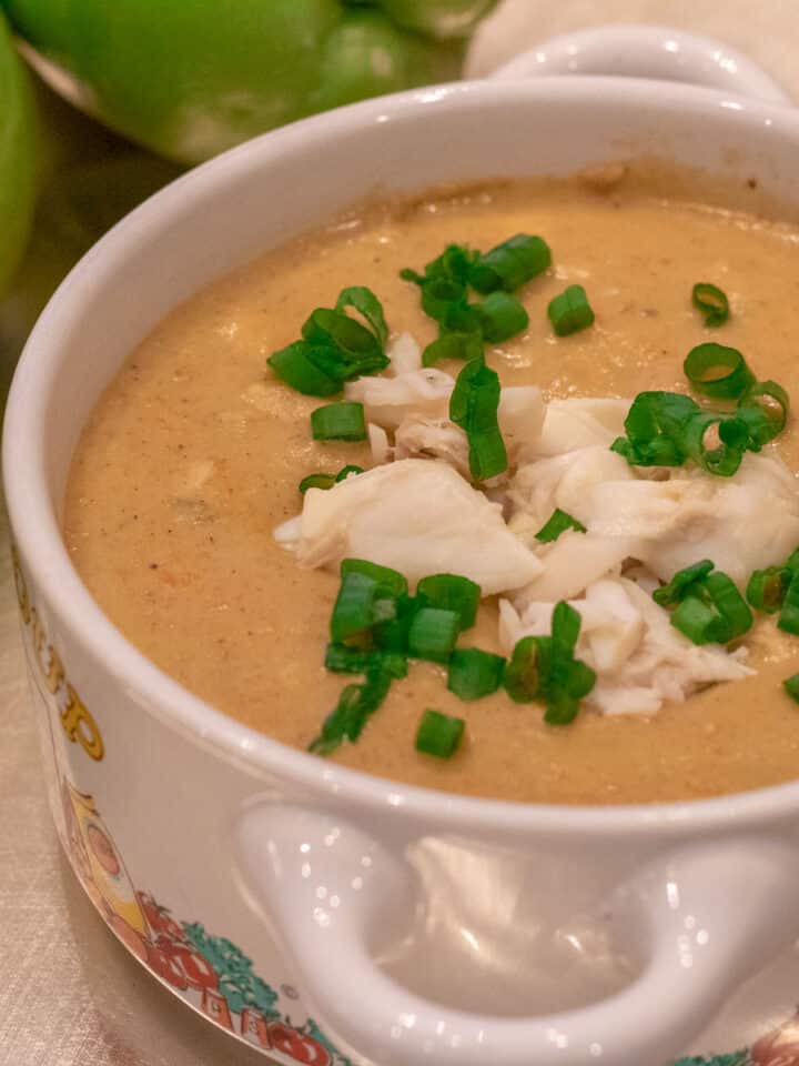 Mirliton crab bisque in a bowl with crabmeat and green onion garnish and whole mirlitons