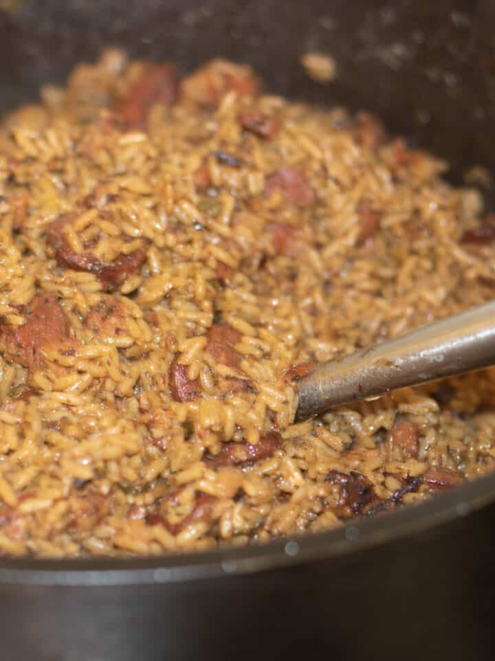 cajun jambalaya with sausage in a large cast iron pot with a serving ladle