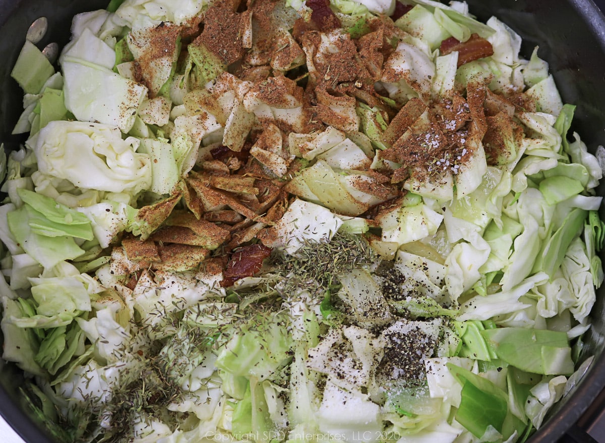 seasonings added in with cabbage and onions in a dutch oven