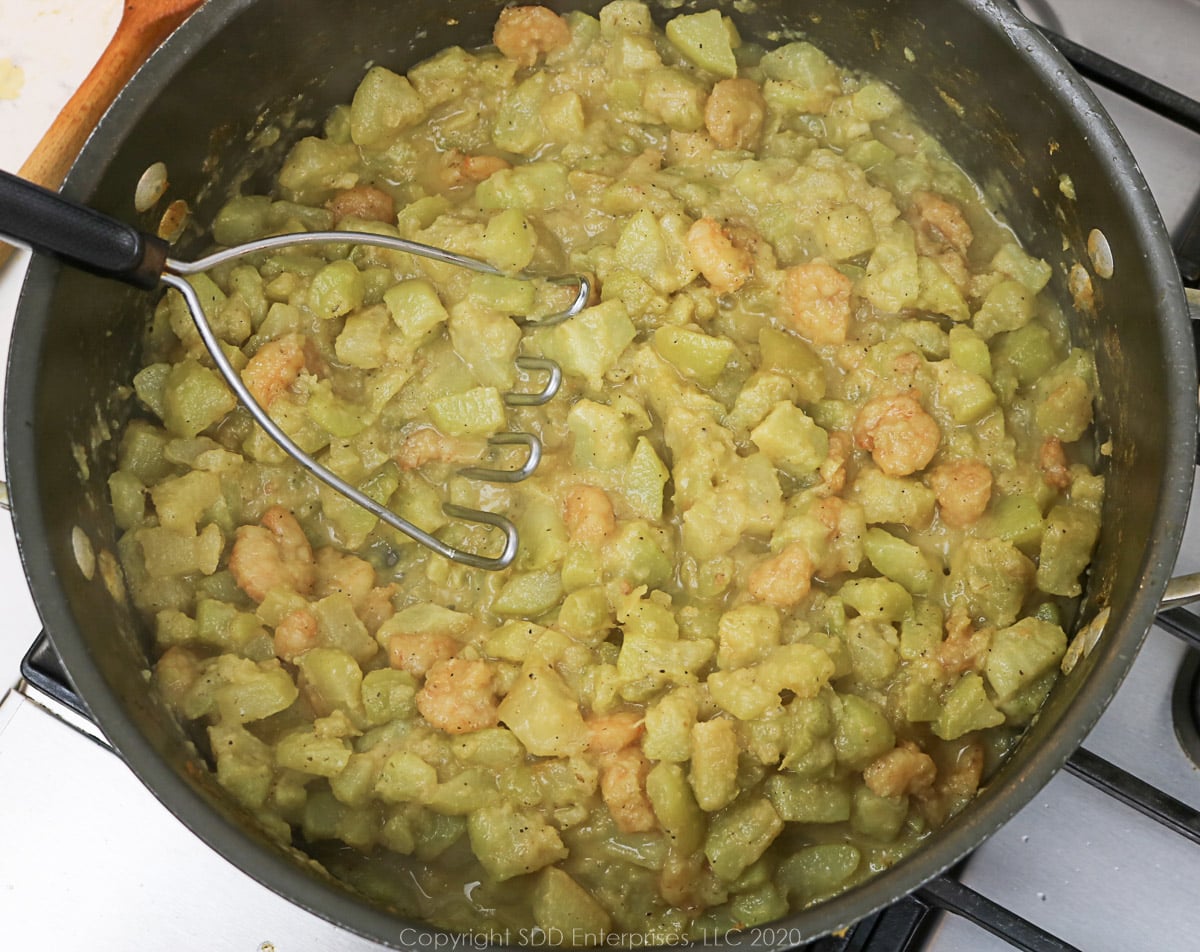 potato masher in chopped mirliton in a Dutch oven