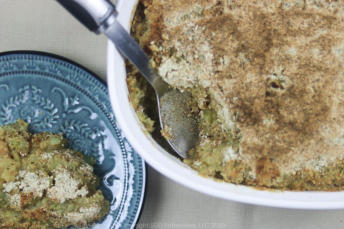 mirliton casserole in a baking dish with serving spoon and a serving on a blue plate