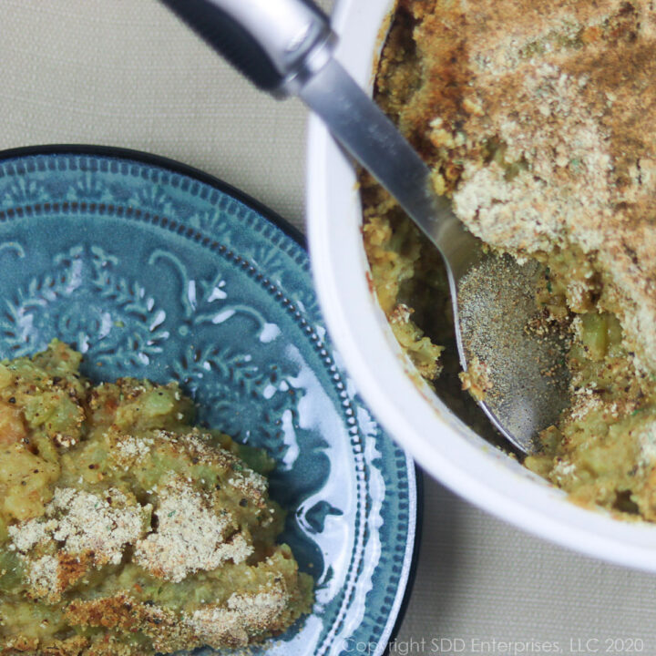 mirliton casserole with shrimp in a white casserole dish with serving spoon and a small blue plate of mirliton casserole on the side