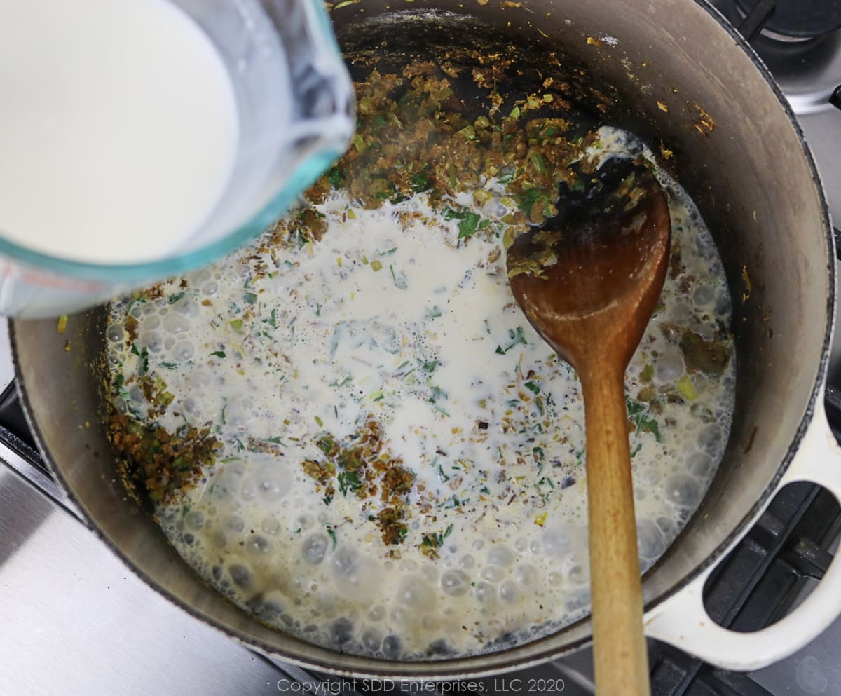 heavy cream being added to roux mixture in a dutch oven