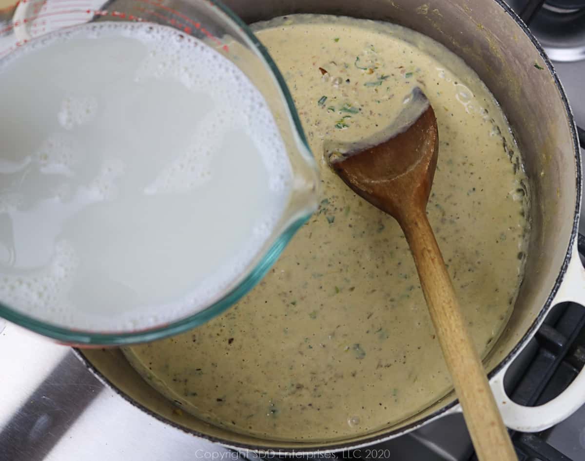 warm milk being added to cream base in a dutch oven