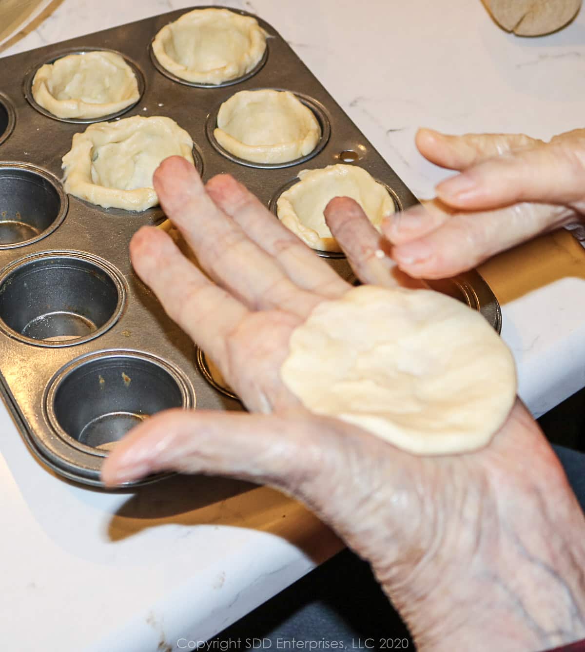 flattened dough going into a mini muffin tin