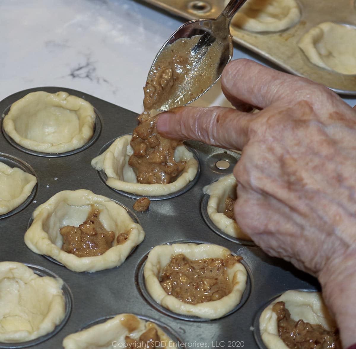 placing pecan filling in individual tart crusts