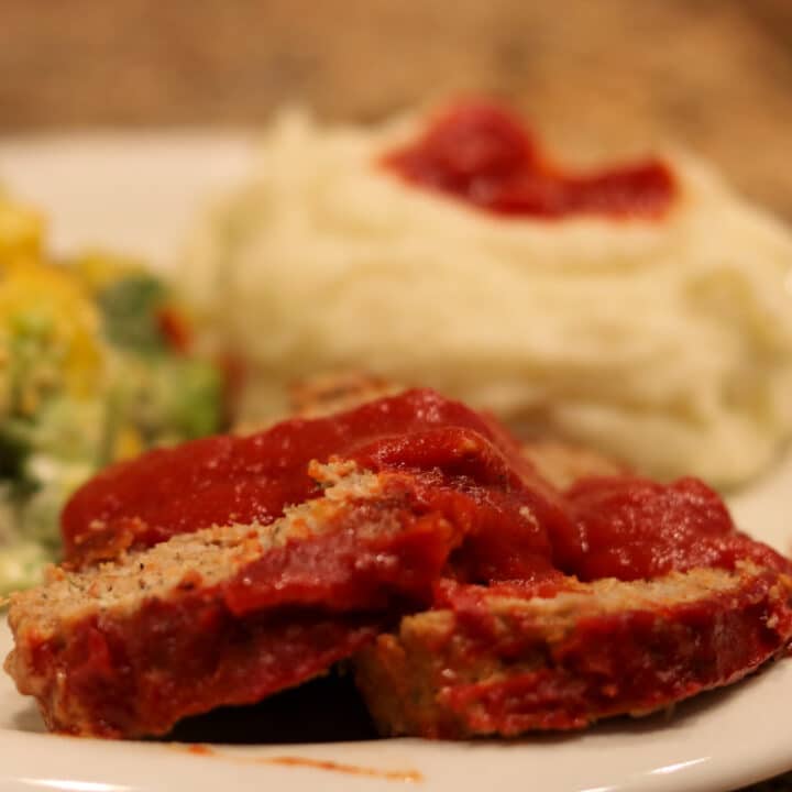 sliced meatloaf with gravy on a plate with mashed potatoes and broccoli