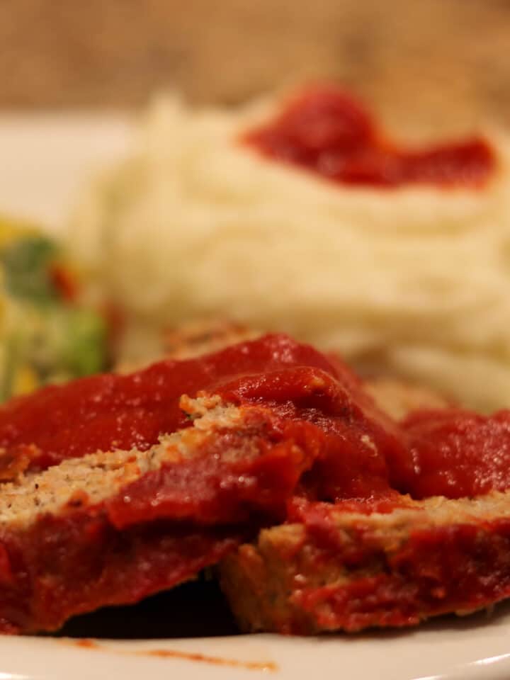 sliced meatloaf with gravy on a plate with mashed potatoes and broccoli