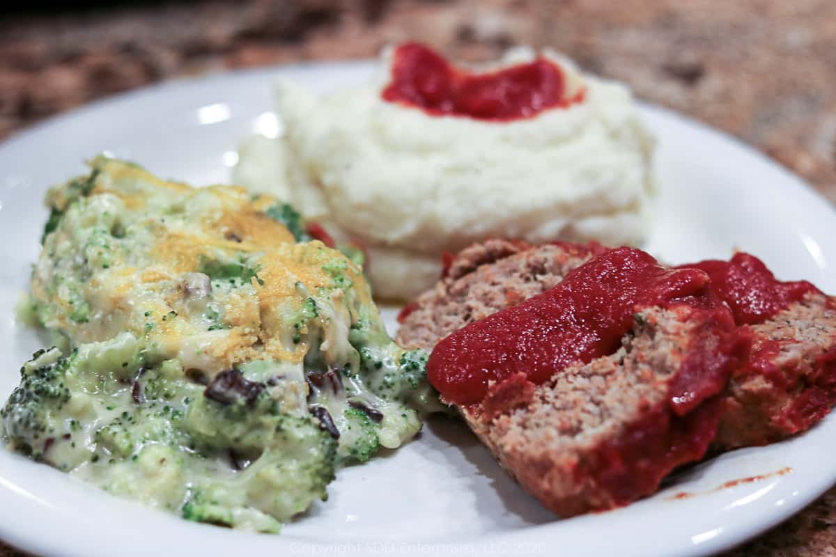 meatloaf with gravy on a plate with mash potatoes and broccoli casserole