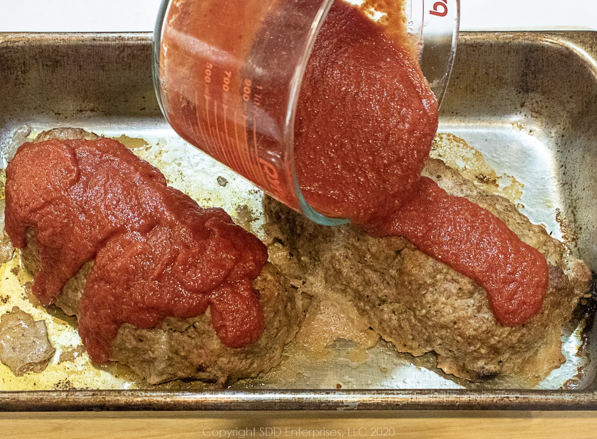 partially baked meatloaves in a baking pan with gravy being applied