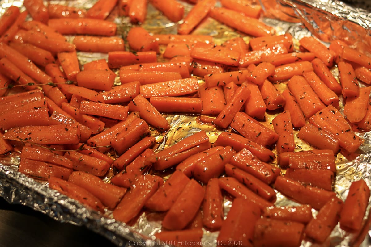 carrots, butter and herbs with cane syrup mix in on a baking sheet