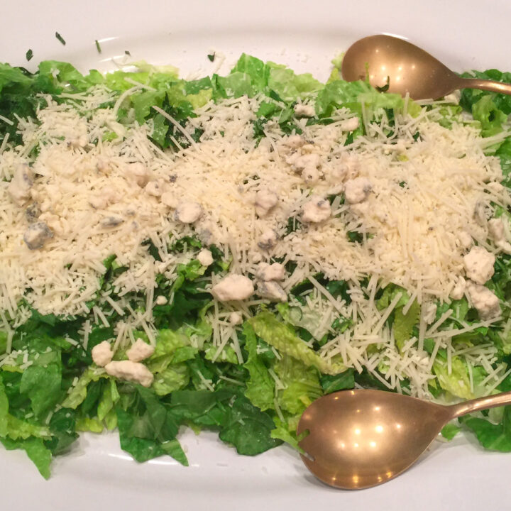 sensation salad with Romano cheese on top and serving spoons on a platter
