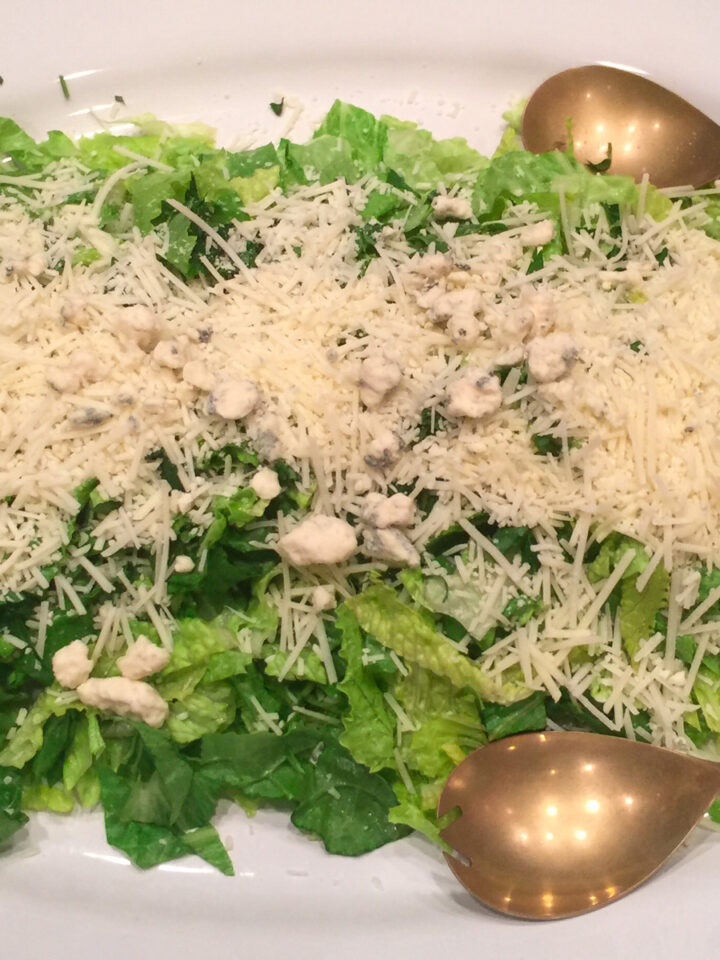 sensation salad with Romano cheese on top and serving spoons on a platter