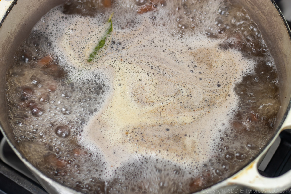 red beans and seasoning meat simmering in a Dutch oven