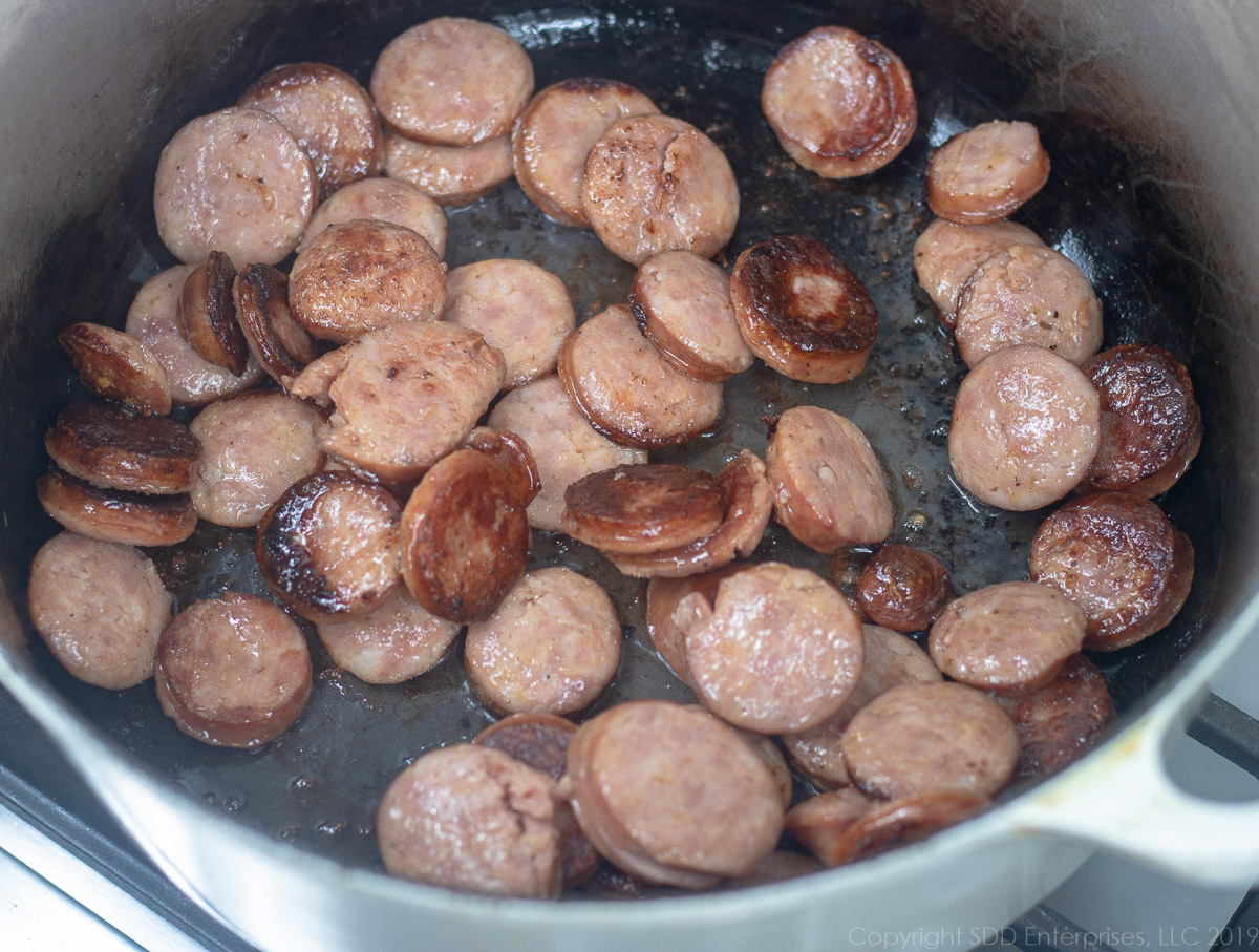 sliced smoke sausage frying in a Dutch oven