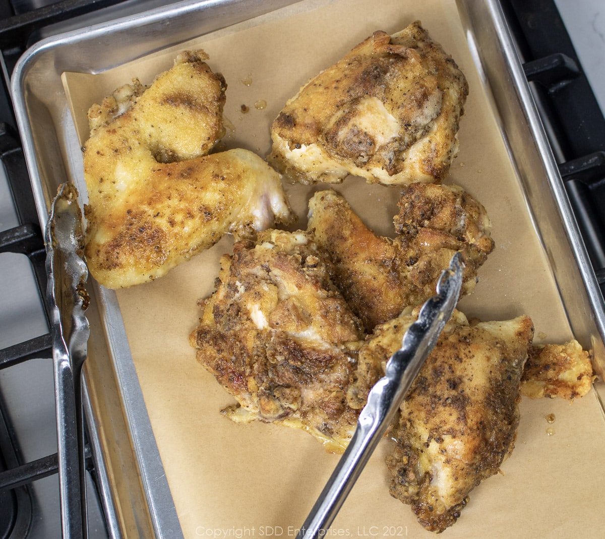 browned chicken on a cooling sheet with tongs