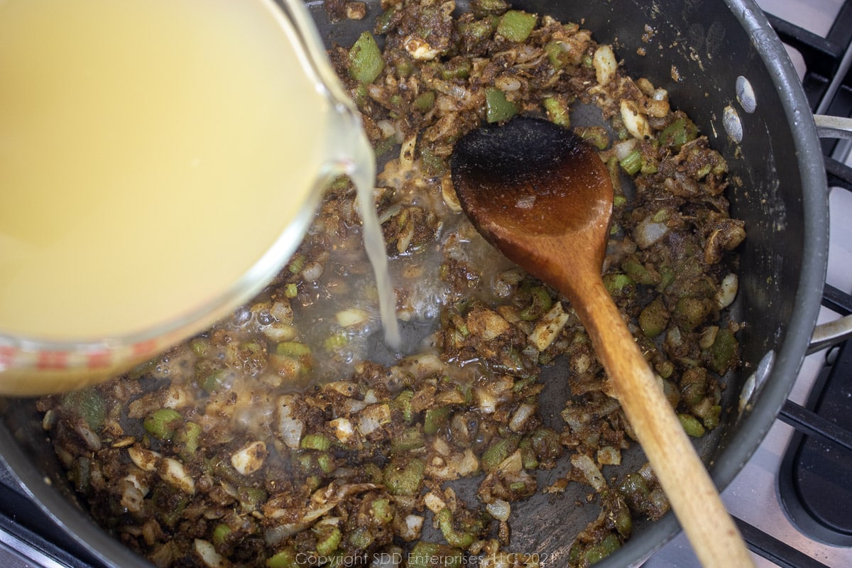 stock being added to vegetables in a roux in a Dutch oven