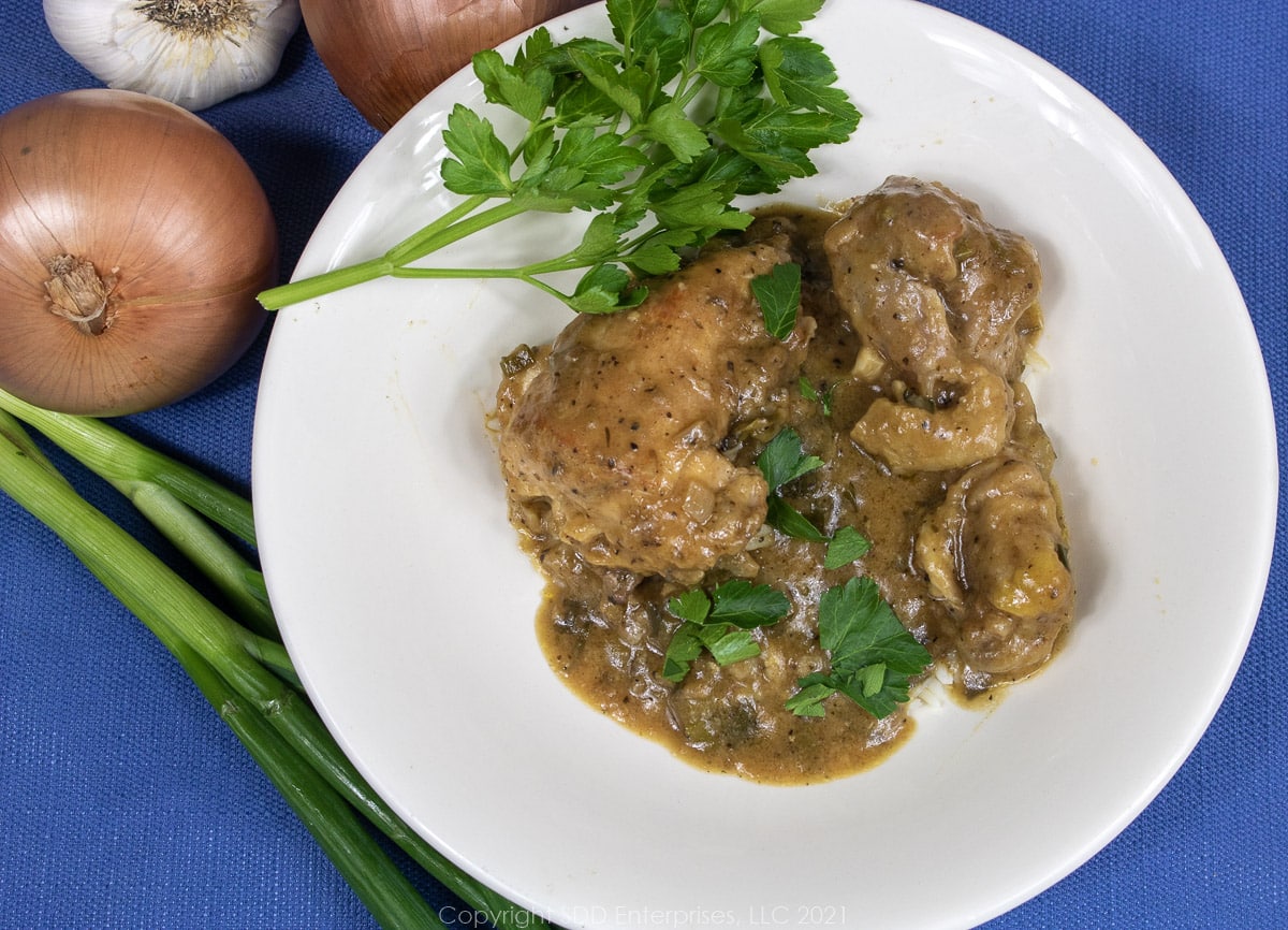 smothered chicken over rice in a white bowl with parsley, green onion, yellow onion and garlic garnish