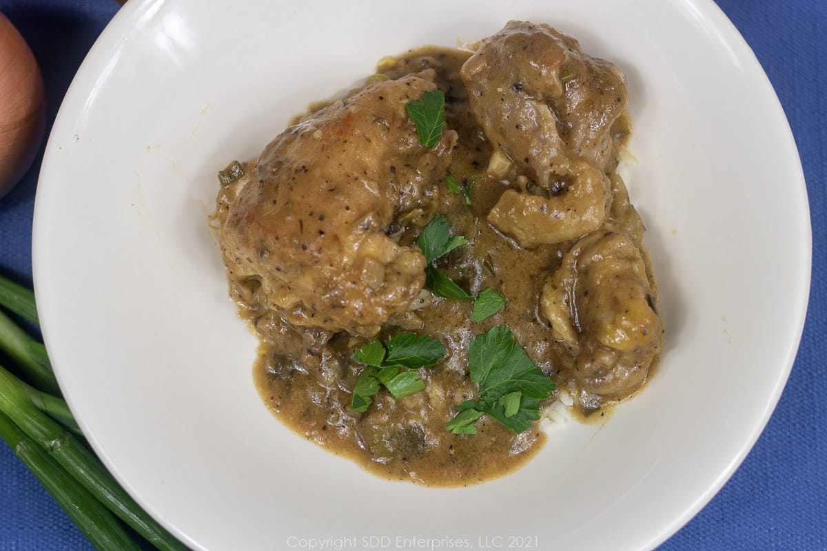 smothered chicken over rice in a white bowl