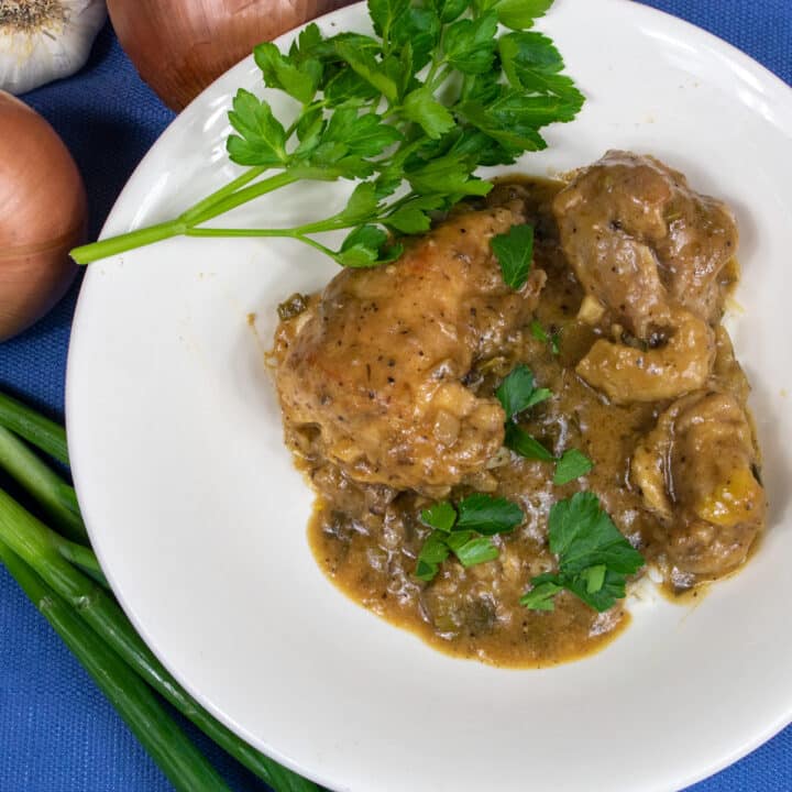 smothered chicken over rice in a white bowl with parsley, green onion, yellow onion and garlic garnish