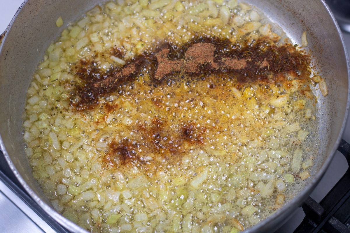 herbs and spices added to yellow onions and garlic in butter in a frying pan