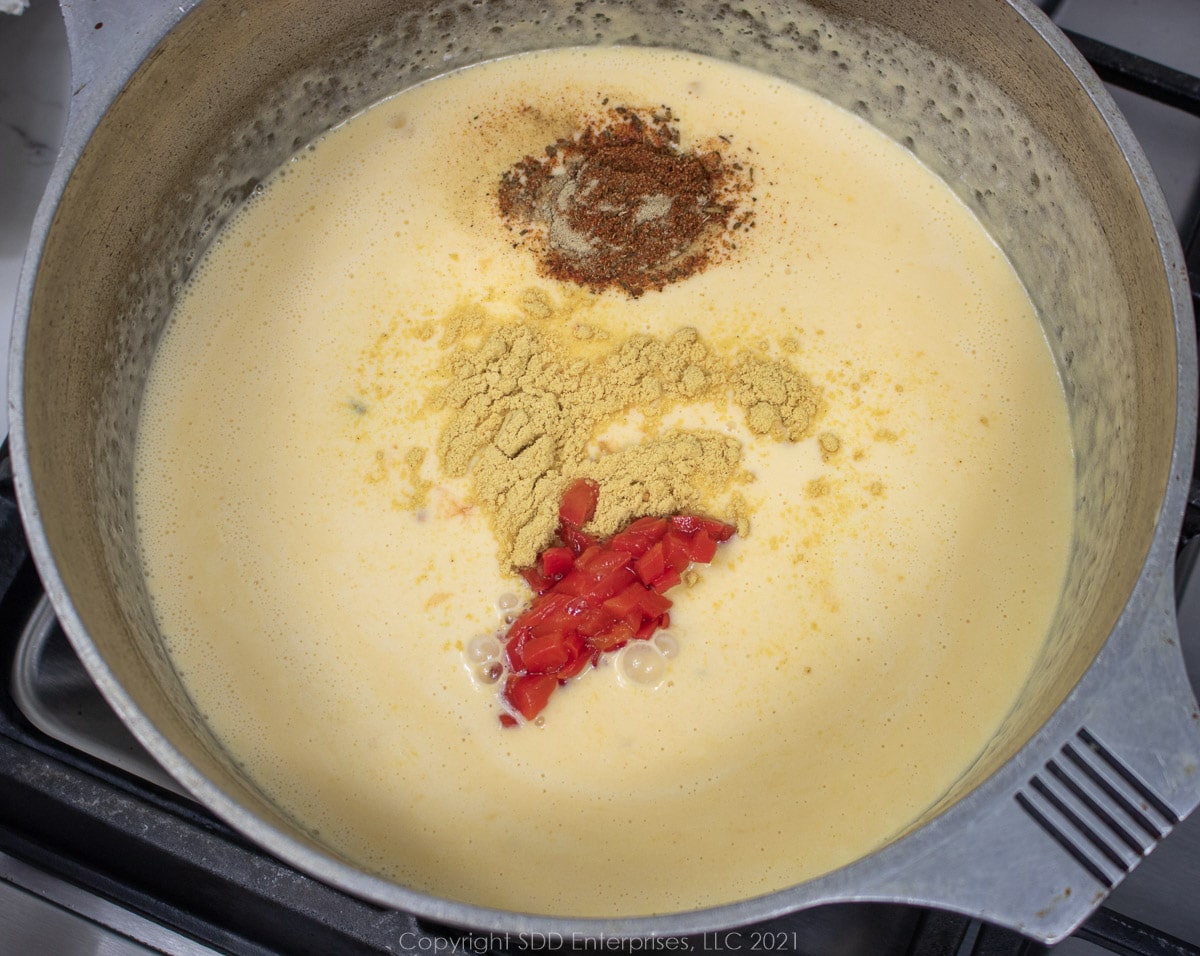 spices and pimentos added to cheese sauce in a Dutch oven