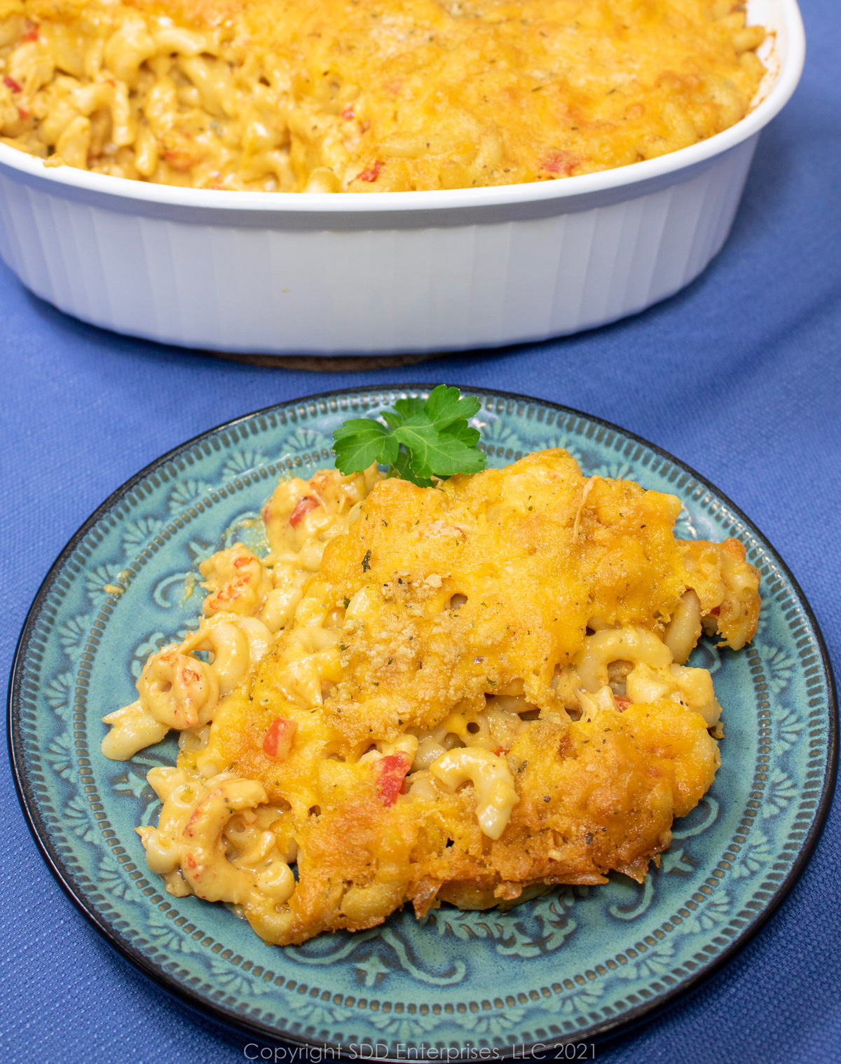 Crawfish macaroni and cheese on a green plate with garnish and a casserole of mac and cheese in the background