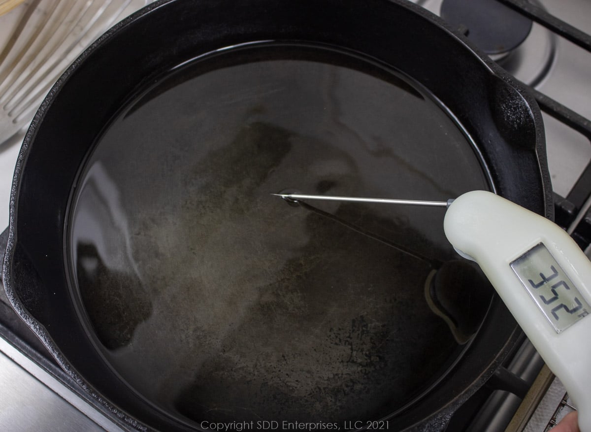 oil being heated in a cast iron skillet and an instant thermometer