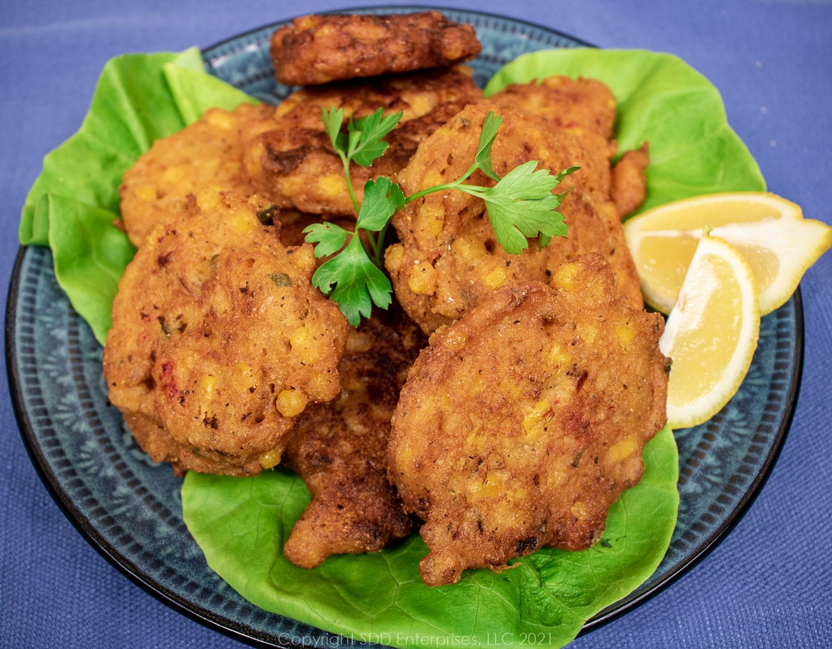 Crawfish and Corn Fritters on a blue-green plate with garnishes