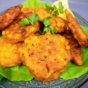 crawfish and corn fritters on a bed of lettuce with parsley and lemon garnish on a blue-green plate