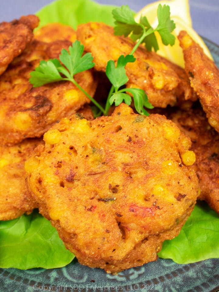 crawfish and corn fritters on a bed of lettuce with parsley and lemon garnish on a blue-green plate