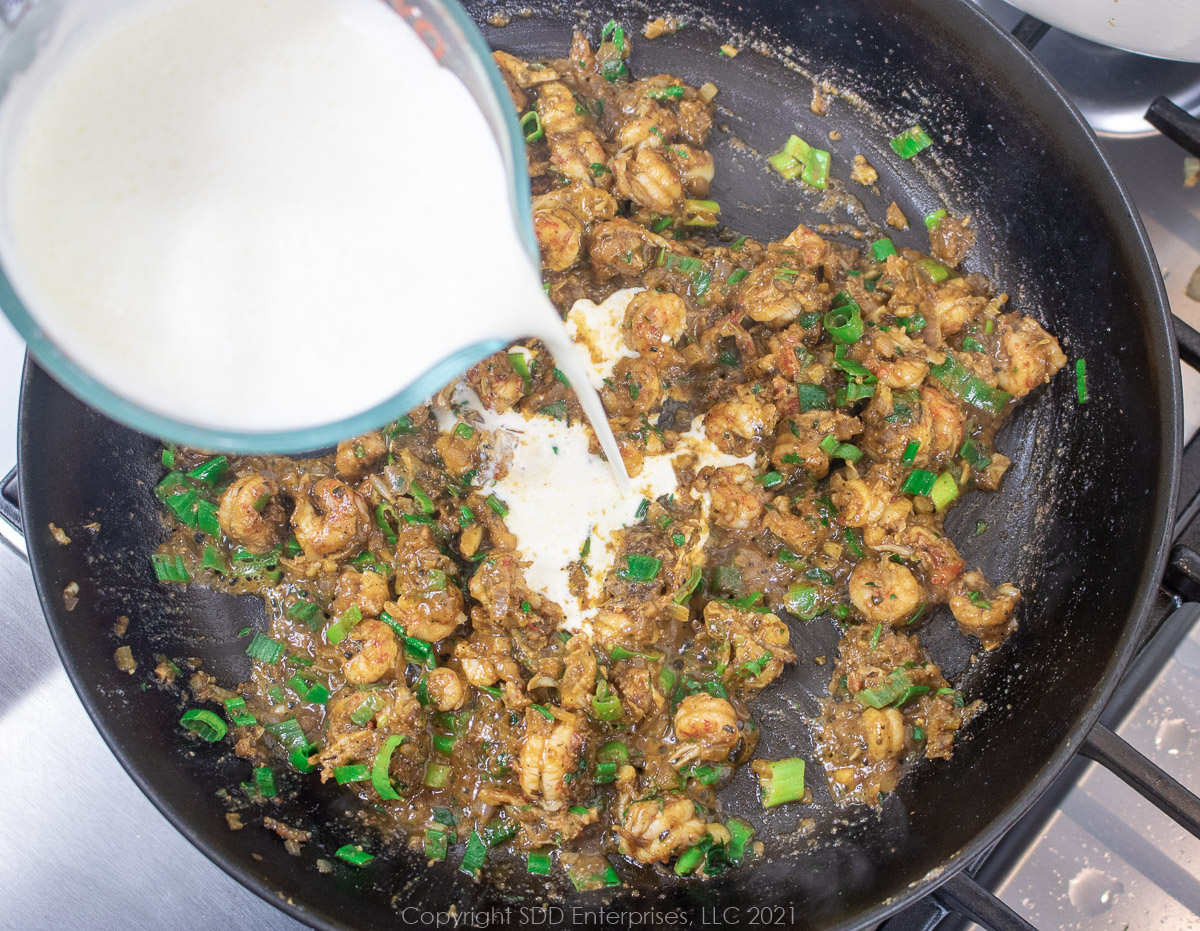 heavy cream being added to sautéing crawfish tails and shallots in a frying pan