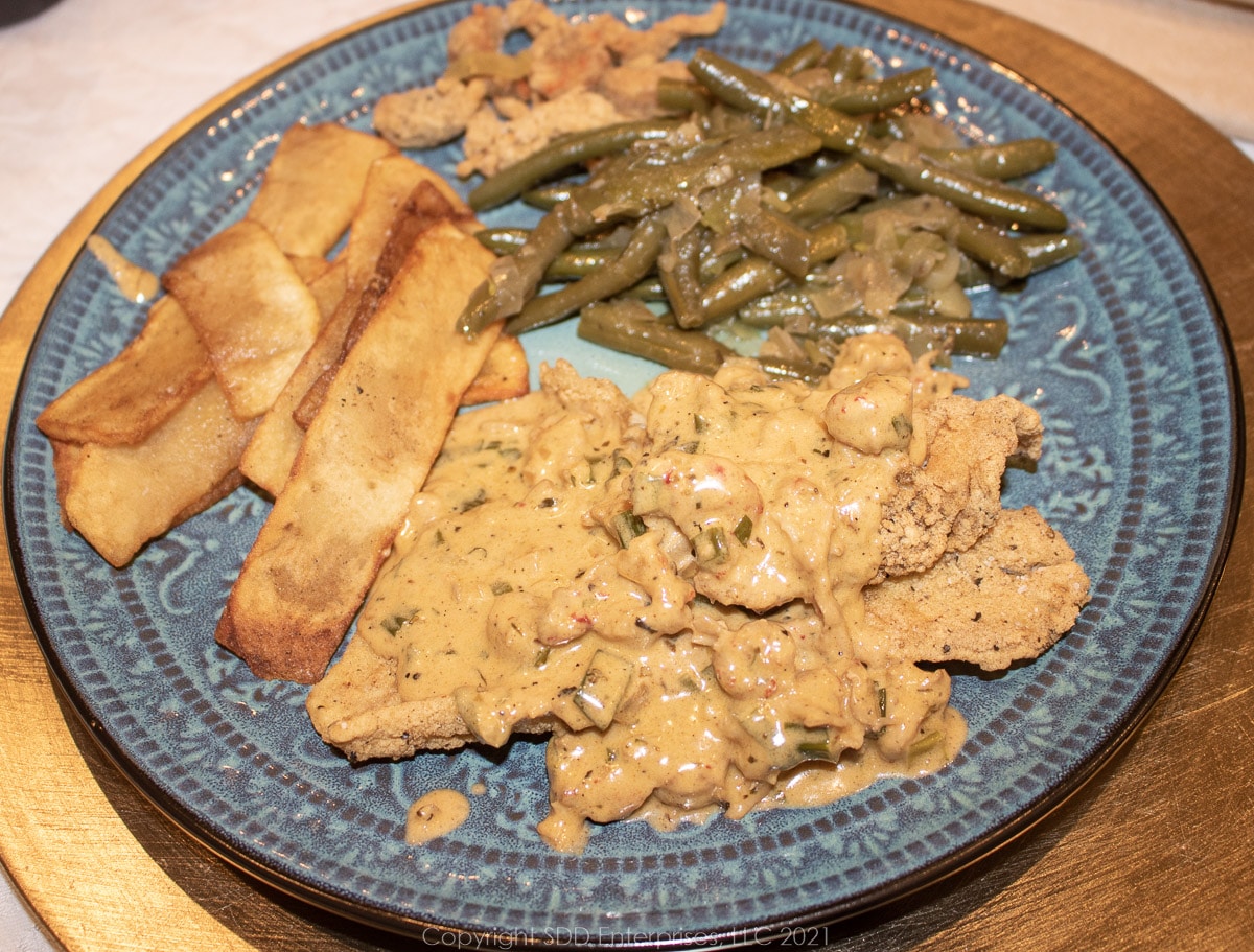 crawfish cream sauce over fried fish with potato and green been sides on a blue-green plate