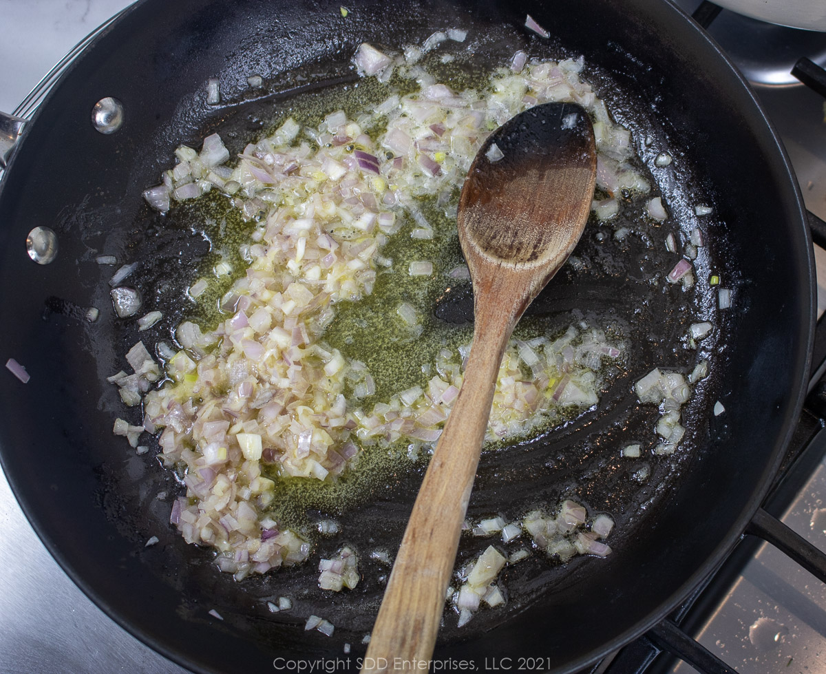 chopped shallots sautéing in ,margarine in a fry pan with a wooden spoon