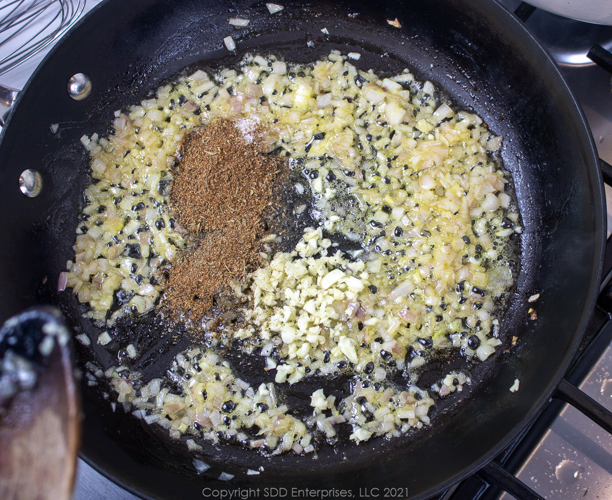 herbs and spices and garlic added to sautéing shallots in a frying pan