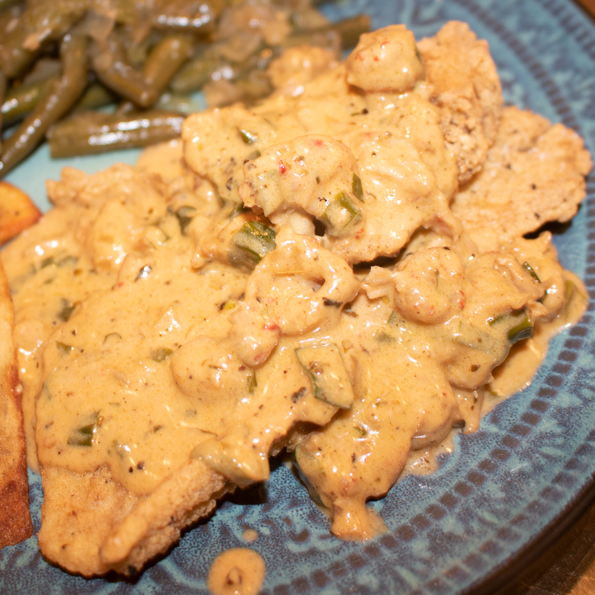 crawfish cream sauce over fried fish with potato and green been sides on a blue-green plate