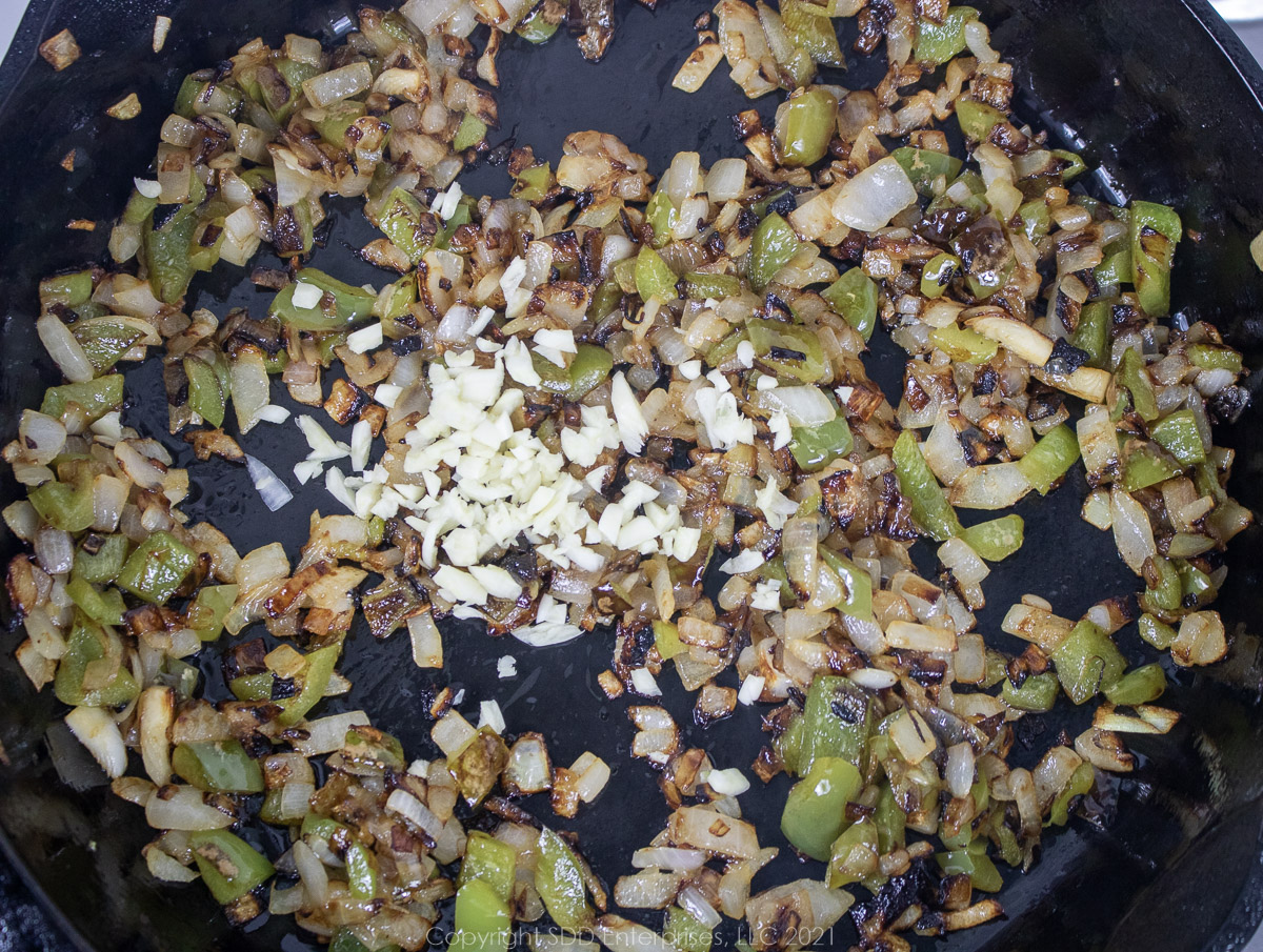 Chopped garlic added to sautéing onions and peppers in a frying pan