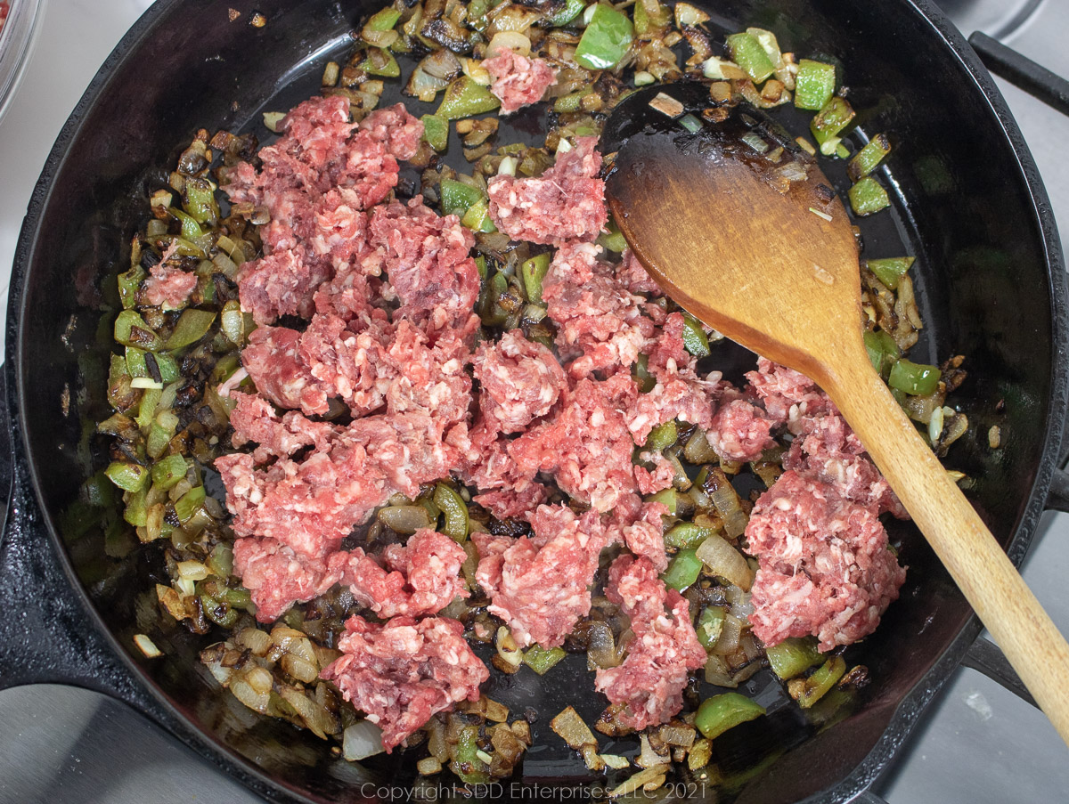 Ground beef crumbled into frying vegetables in a cast iron frying pan
